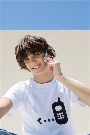 simsearch:695-05768222,k - Teenage boy wearing tee-shirt printed with cell phone graphic, using cell phone, smiling at camera Foto de stock - Sin royalties Premium, Código: 695-05767881