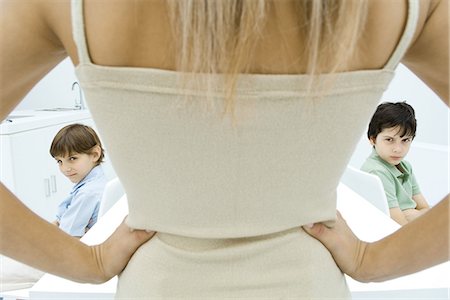 pouting - Mother standing with hands on hips, rear view, boys sulking in background, cropped view Stock Photo - Premium Royalty-Free, Code: 695-05768029