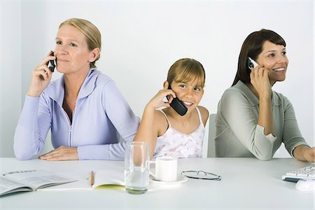 Mother and two daughters sitting at table, each using cell phone, smiling Stock Photo - Premium Royalty-Free, Code: 695-05768091