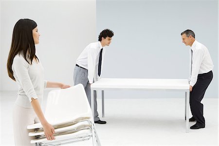 Professionals setting up office, men moving table, woman carrying chairs Stock Photo - Premium Royalty-Free, Code: 695-05768102