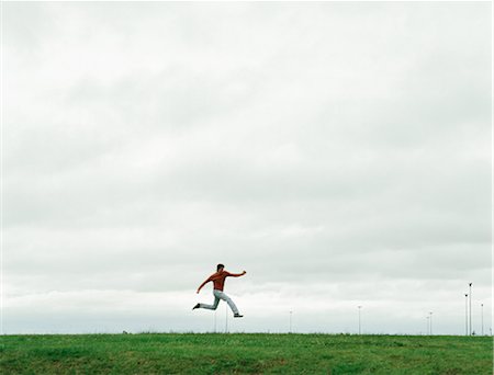 Man jumping on grassy field, in the distance Stock Photo - Premium Royalty-Free, Code: 695-05768117