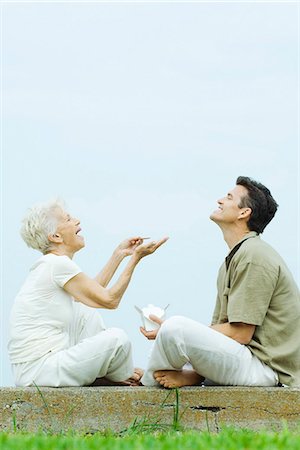 Senior woman and adult son sitting face to face on the ground, sharing takeout food, laughing Stock Photo - Premium Royalty-Free, Code: 695-05768182