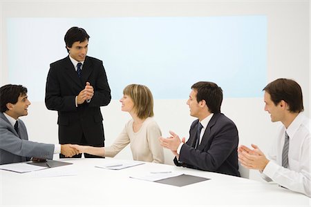 Business associates at conference table, two shaking hands, the others clapping Stock Photo - Premium Royalty-Free, Code: 695-05768197