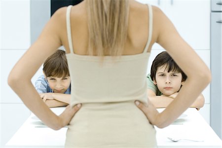 Boys pouting at kitchen table, being disciplined by mother, rear view Stock Photo - Premium Royalty-Free, Code: 695-05768257