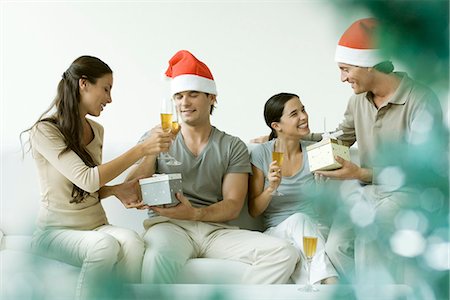 Two couples exchanging Christmas gifts, drinking champagne, men wearing Santa hats Stock Photo - Premium Royalty-Free, Code: 695-05768276