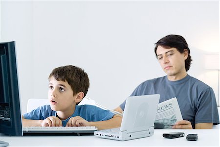 Little boy computer and portable DVD player, father reading newspaper in background Stock Photo - Premium Royalty-Free, Code: 695-05768385