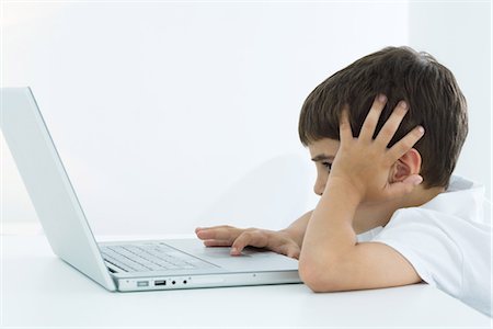 person and lap top and cut out - Little boy using laptop computer, holding head, side view Stock Photo - Premium Royalty-Free, Code: 695-05768388