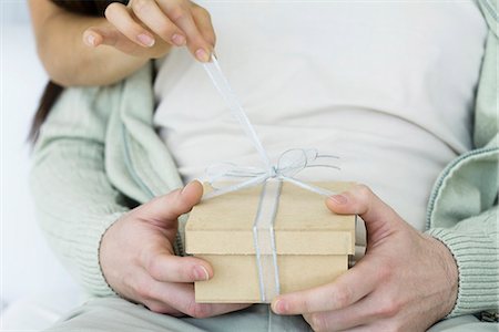 simsearch:695-05768442,k - Man holding gift, woman's arm reaching around to untie the ribbon, cropped view Stock Photo - Premium Royalty-Free, Code: 695-05768454