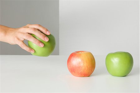 picking hand - Hand picking up an apple, two other apples sitting in a row, cropped view Stock Photo - Premium Royalty-Free, Code: 695-05768467