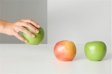 picking apples - Hand picking up an apple, two other apples sitting in a row, cropped view Stock Photo - Premium Royalty-Free, Code: 695-05768467