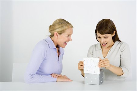 Woman opening gift, another woman sitting nearby watching, both excited Stock Photo - Premium Royalty-Free, Code: 695-05768492