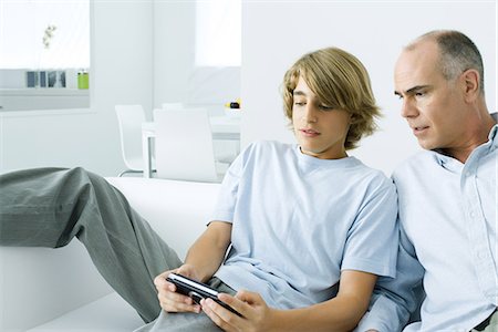 sitting holding legs up - Teen boy playing handheld video game, father watching over his shoulder Stock Photo - Premium Royalty-Free, Code: 695-05768539