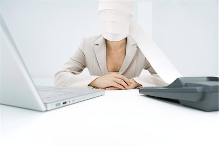 Professional woman sitting at desk, paper from adding machine wrapped around face Stock Photo - Premium Royalty-Free, Code: 695-05768557