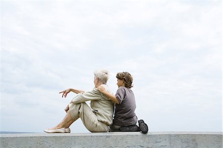 picture of woman kneeling down from behind - Grandmother and grandson sitting together on low wall outdoors, looking at view Stock Photo - Premium Royalty-Free, Code: 695-05768603