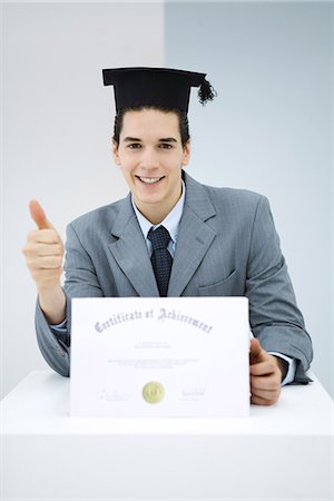 Young man with diploma, wearing graduation cap, making thumbs-up gesture Fotografie stock - Premium Royalty-Free, Codice: 695-05768815