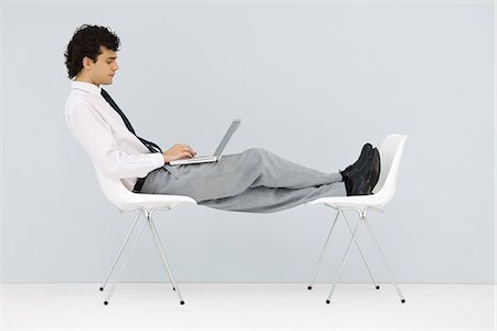 Homme assis dans la chaise, les pieds vers le haut sur une autre chaise, en utilisant un ordinateur portable Photographie de stock - Premium Libres de Droits, Code: 695-05768819