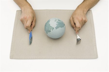 Person sitting before globe on placemat, holding fork and knife, cropped view Stock Photo - Premium Royalty-Free, Code: 695-05768942