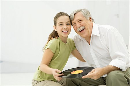 Grandfather and granddaughter holding record album together, smiling, portrait Stock Photo - Premium Royalty-Free, Code: 695-05769034