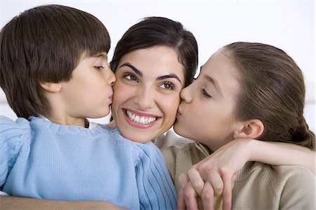 Portrait of smiling mother being kissed on each cheek by young daughter and son Stock Photo - Premium Royalty-Free, Code: 695-05769087