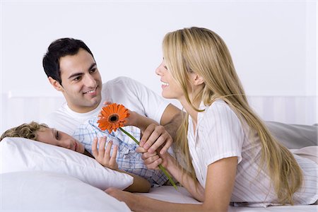 simsearch:695-05769105,k - Family relaxing together on bed, woman holding flower Stock Photo - Premium Royalty-Free, Code: 695-05769106