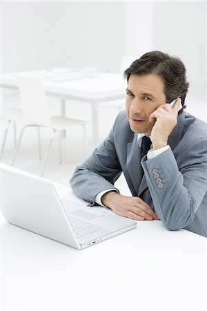 Businessman talking on cell phone, sitting by laptop computer Stock Photo - Premium Royalty-Free, Code: 695-05769140