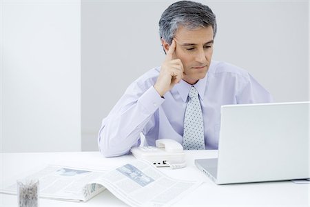 Businessman sitting at desk, looking at laptop computer, holding head Stock Photo - Premium Royalty-Free, Code: 695-05769178