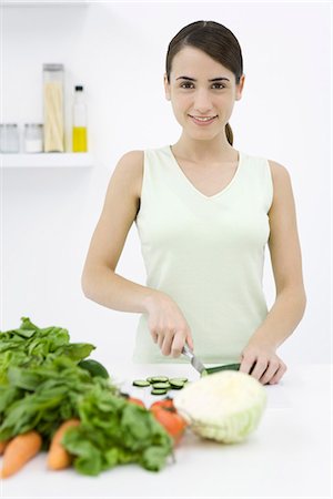 Woman slicing cucumber, assorted vegetables in foreground, smiling at camera Stock Photo - Premium Royalty-Free, Code: 695-05769226