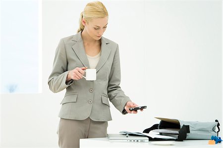 Professional woman holding coffee cup, looking down, text messaging Stock Photo - Premium Royalty-Free, Code: 695-05769240