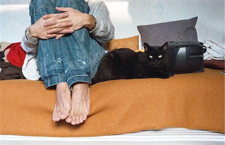 Jeune homme assis sur le lit s'enlaçant à genoux, chat couché à côté Photographie de stock - Premium Libres de Droits, Code: 695-05769361