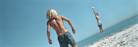 Friends throwing frisbee at beach, one jumping to catch frisbee Stock Photo - Premium Royalty-Free, Code: 695-05769879