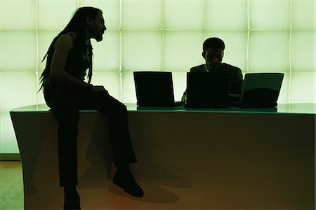 desk dark - Man with dreadlocks sitting on desk speaking to businessman using laptop computer Stock Photo - Premium Royalty-Free, Code: 695-05769915