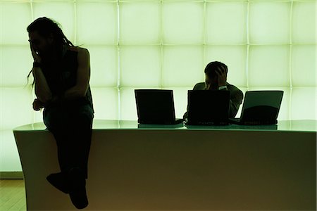 desk dark - Man with dreadlocks sitting on desk, hand under chin, businessman using laptop computer Stock Photo - Premium Royalty-Free, Code: 695-05769916