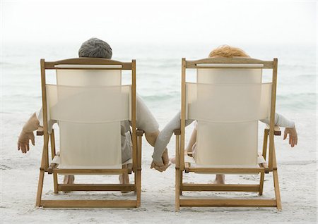 Couple sitting in beach chairs, holding hands, rear view Stock Photo - Premium Royalty-Free, Code: 695-05762933