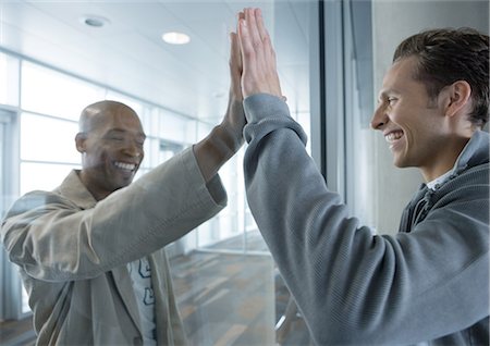 Two men holding up hands on either side of glass in airport, laughing Stock Photo - Premium Royalty-Free, Code: 695-05763308