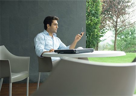 Man sitting at table outdoors, looking at cell phone Stock Photo - Premium Royalty-Free, Code: 695-05763795