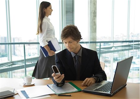 simsearch:695-03381633,k - Businessman looking at cell phone, woman walking by in background Stock Photo - Premium Royalty-Free, Code: 695-05763880