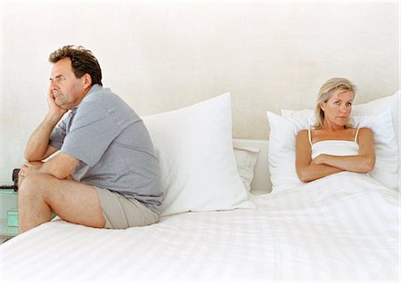 Woman in bed with arms crossed, man sitting on side of bed Stock Photo - Premium Royalty-Free, Code: 695-05774017