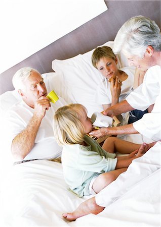 Grandparents and children eating breakfast on bed, woman helping little girl drink from mug Stock Photo - Premium Royalty-Free, Code: 695-05774027