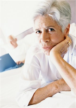 simsearch:695-05774214,k - Senior woman on bed with hand under chin, man using laptop in background Stock Photo - Premium Royalty-Free, Code: 695-05774052