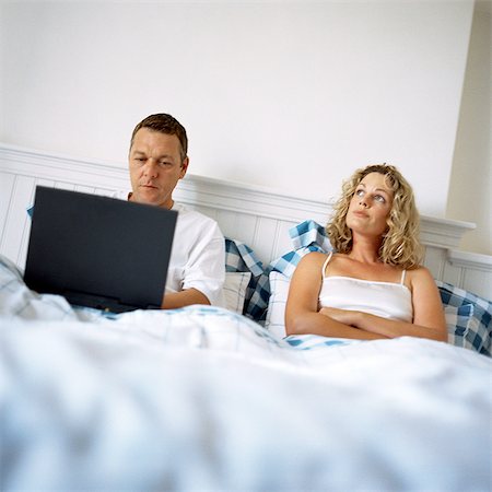 simsearch:695-05774214,k - Couple in bed, man using laptop computer, woman with arms crossed Stock Photo - Premium Royalty-Free, Code: 695-05774214