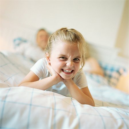 Girl lying at end of parent's bed, making face Stock Photo - Premium Royalty-Free, Code: 695-05774226