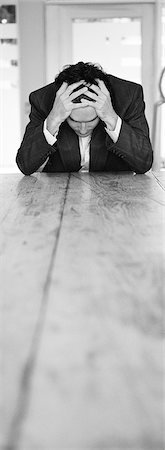 simsearch:695-05772340,k - Man sitting at end of table holding head in hands, b&w, vertical Foto de stock - Royalty Free Premium, Número: 695-05774746