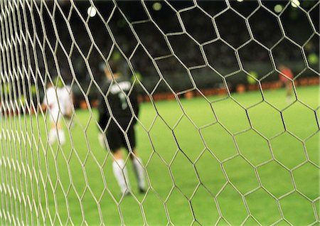 Goal keeper standing in front of goal during a match, blurred, seen from behind net. Stock Photo - Premium Royalty-Free, Code: 695-05775844
