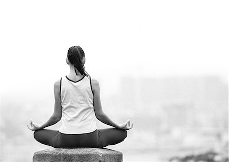Woman sitting in yoga position, overlooking city, rear view, blurred, focus on foreground, b&w Stock Photo - Premium Royalty-Free, Code: 695-05775880
