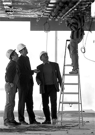 Three men with hard hats looking at man on stepladder, b&w Stock Photo - Premium Royalty-Free, Code: 695-05776085