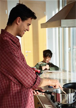 divorced family - Father cooking, son in background looking at book. Stock Photo - Premium Royalty-Free, Code: 695-05776727