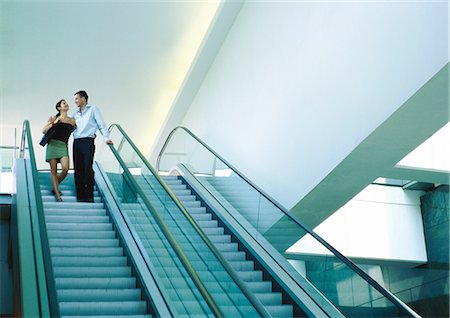 Couple riding down escalator, smiling Stock Photo - Premium Royalty-Free, Code: 695-05776951