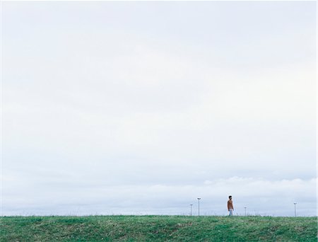 people walking in the distance - Young man in distance standing on grass under overcast sky Stock Photo - Premium Royalty-Free, Code: 695-05777296