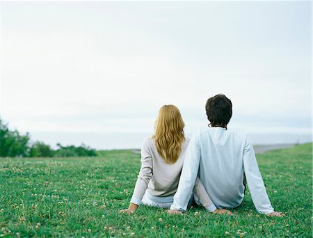 Young man and young woman sitting side by side on grass, propped up with hands, rear view Stock Photo - Premium Royalty-Free, Code: 695-05777319
