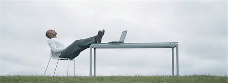 still technology concept - Man sitting in chair outdoors with feet on table and laptop on table, in front of overcast sky Stock Photo - Premium Royalty-Free, Code: 695-05777334